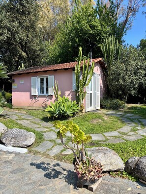 A pink building with white shutters, surrounded by a garden with large rocks and cacti.