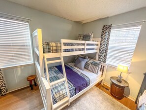 A bunk bed room with patterned bedding, a small stool, and a lamp.