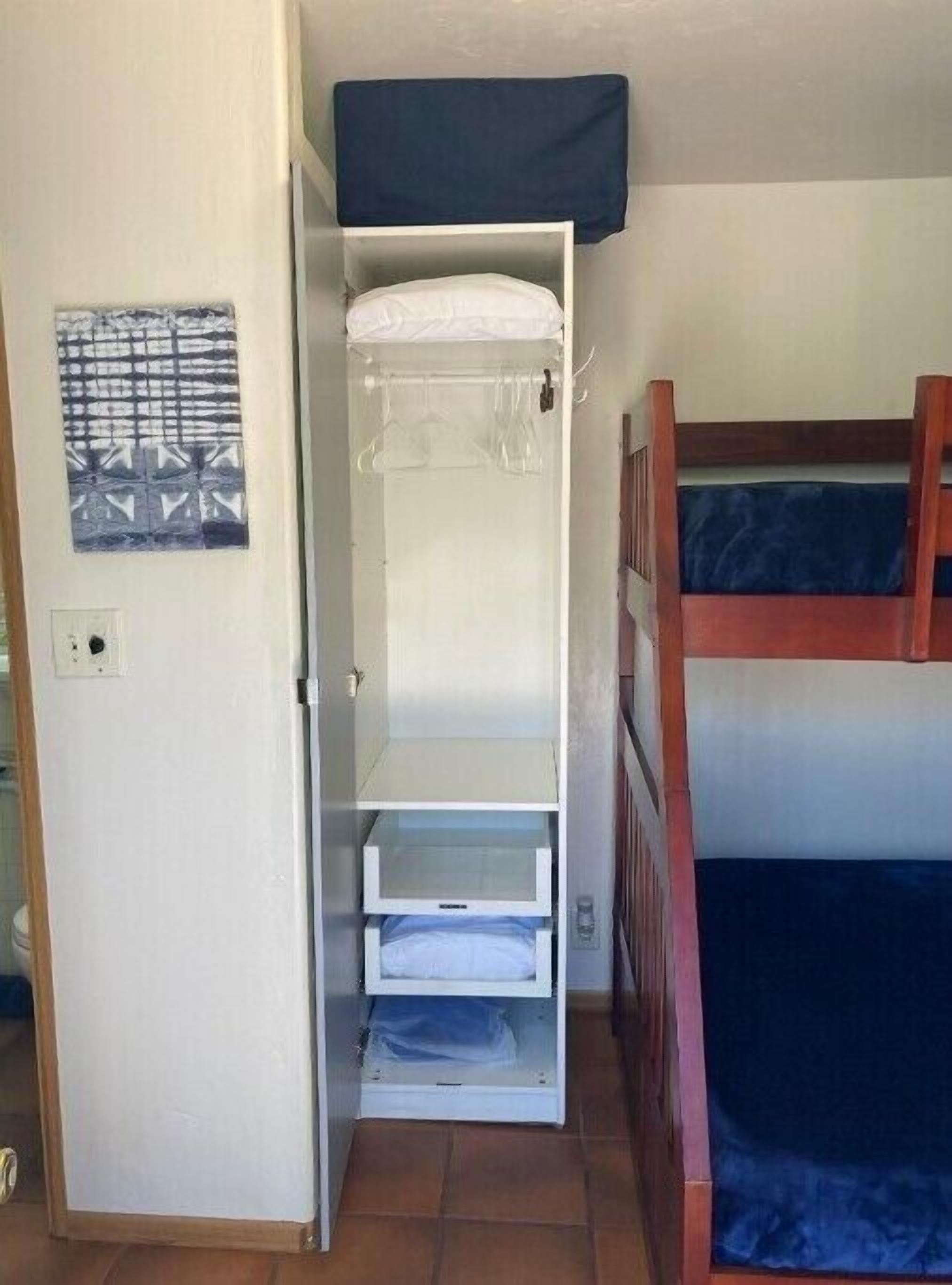 A compact room with a bunk bed, a wardrobe with open shelves, and a patterned wall hanging.