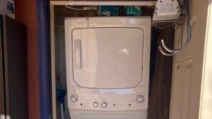 A compact laundry room with a washing machine and dryer, a small window, and a door with a metal handle. - Charming Casita in Historic Barrio Viejo 144 sq ft. (Tucson)