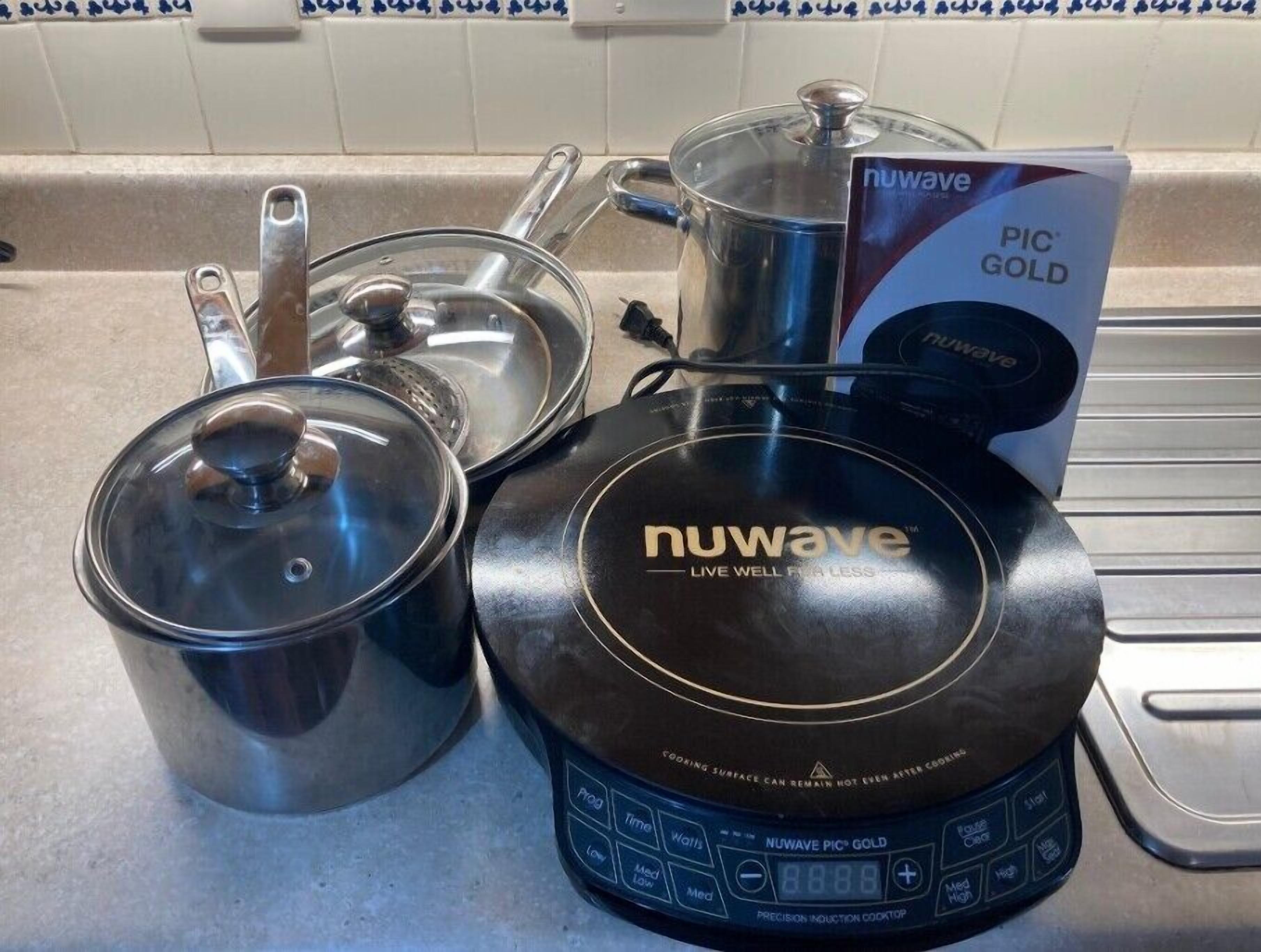 A Nuwave PIC GOLD induction cooktop with a digital display, a stainless steel pot with a lid, and a glass lid pot on a kitchen counter.