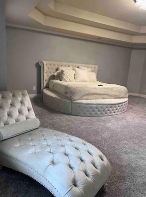 Un dormitorio con cama y cabecera capitonada, un sillón capitonado y suelo alfombrado.