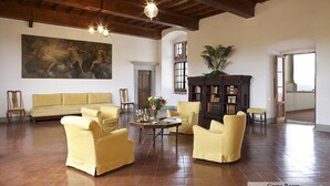 A spacious room with a large painting, a sofa, yellow armchairs, a wooden coffee table, and a bookshelf. - Castello Lorenzo Heart of Tuscany Renaissance Villa With Pool (San Casciano in Val di Pesa)