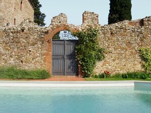 A stone building with a metal gate, a pool, and greenery.