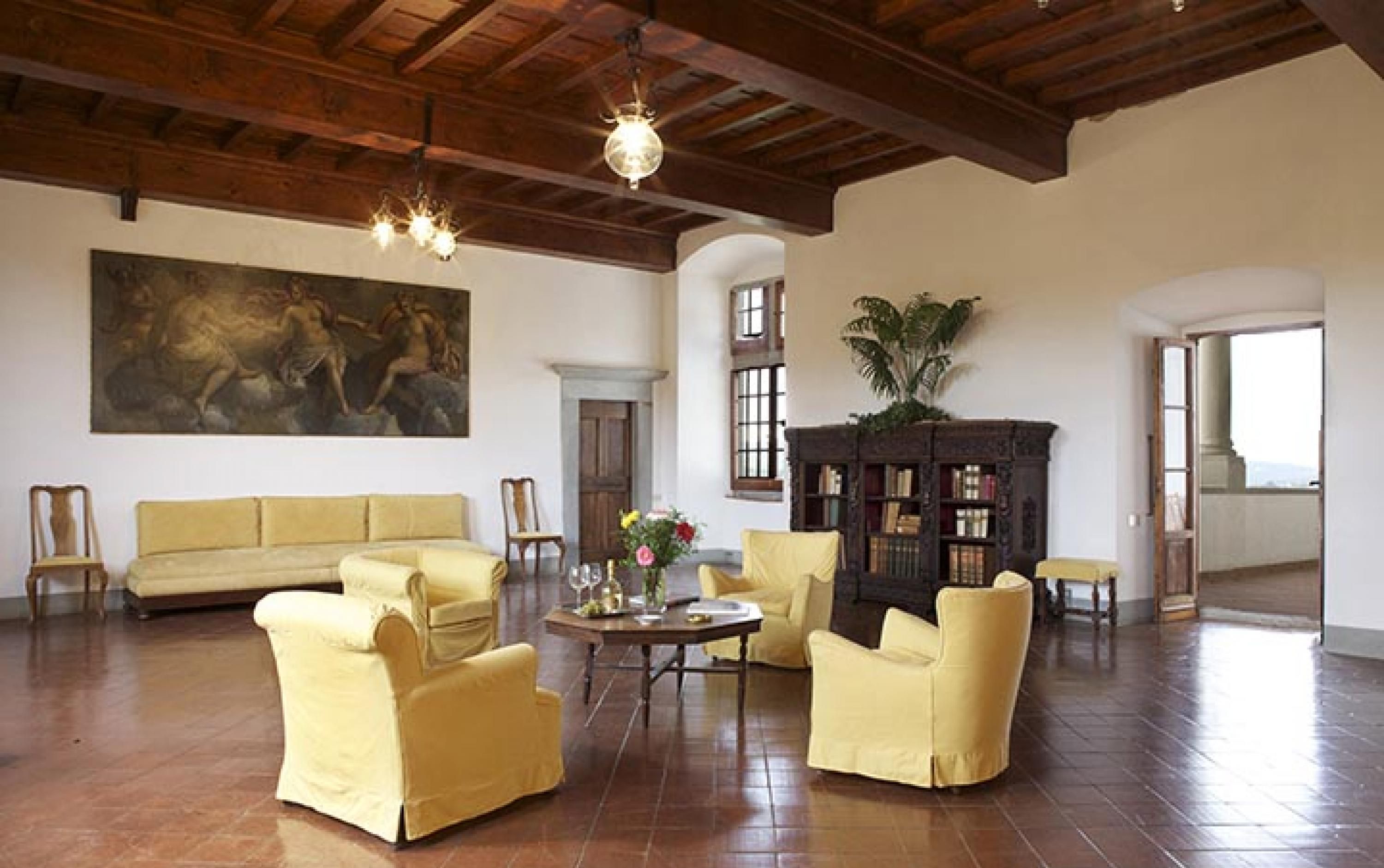 Una habitación amplia con un cuadro grande, un sofá, sillones amarillos, una mesa de centro de madera y una estantería.