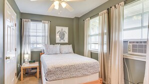 Ein Schlafzimmer mit einem Bett, einem Deckenventilator, einem Nachttisch mit Lampe und einer Wand-Klimaanlage.