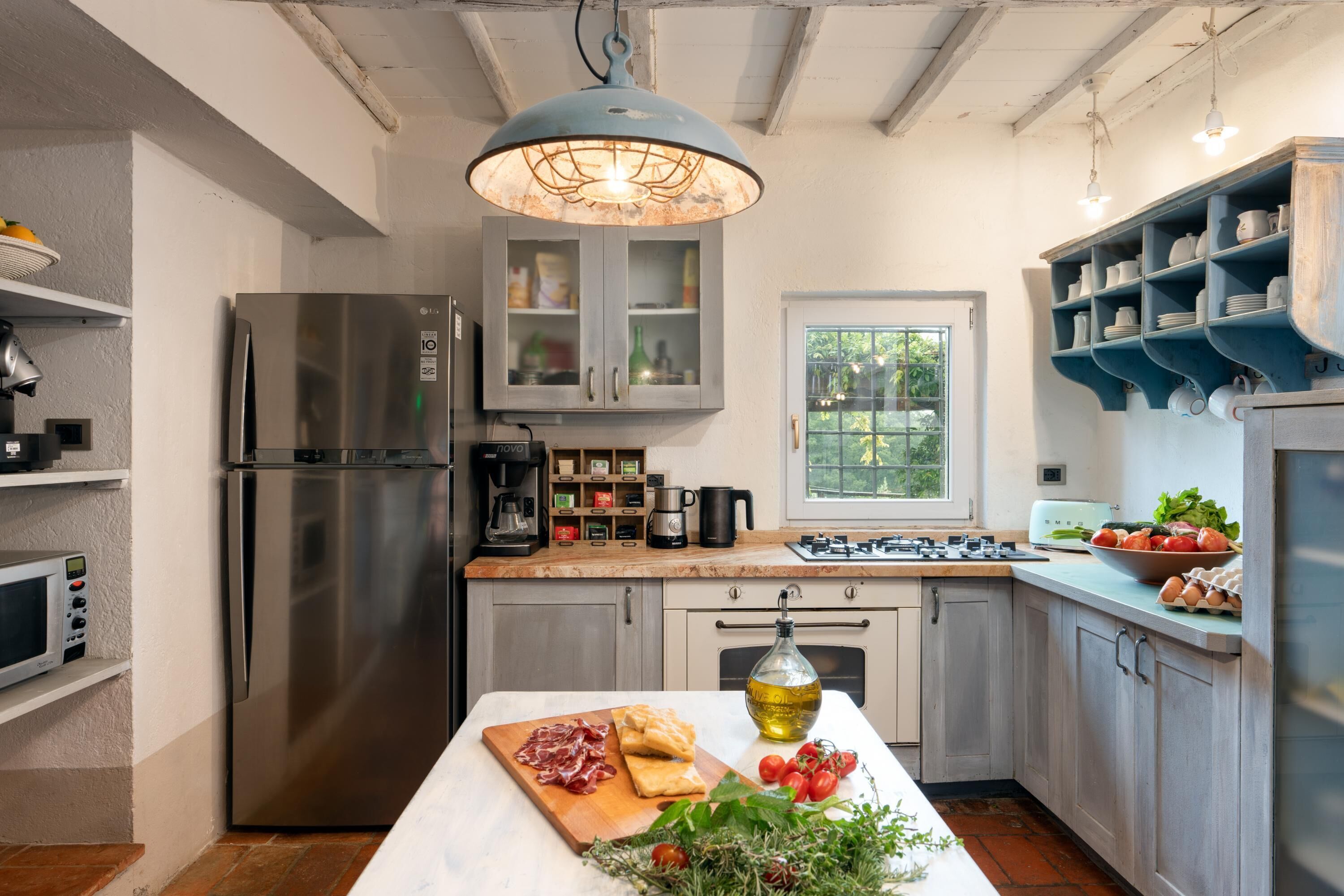 Una cucina moderna con un frigorifero in acciaio inossidabile, un'isola centrale con frutta e verdura fresca, e una lampada a sospensione blu.