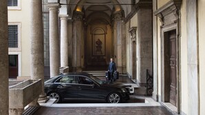 Une voiture noire est garée dans un couloir orné de colonnes, d’un buste sculpté et d’une porte dotée d’un cadre décoratif.