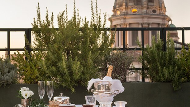 Un espace de restauration en plein air avec une table dressée pour deux personnes, offrant une vue sur un bâtiment historique doté d’un dôme.
