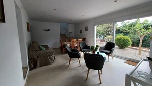 A modern living room with a sofa, two black chairs, and a dining table. There is a staircase leading to an upper floor, and a large glass door opens to a garden. - Magnifica Casa CON Piscina Privada Y Vistas AL MAR (L'Escala)
