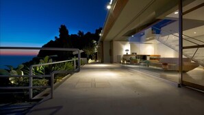 A modern building with a glass facade, a staircase, and a view of the ocean. - Favoloso - Argentario Tuscany Stunning Modern Seaside Villa Private Pool Access to Sea (Monte Argentario)