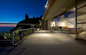 A modern building with a glass facade, a staircase, and a view of the ocean. - Favoloso - Argentario Tuscany Stunning Modern Seaside Villa Private Pool Access to Sea (Monte Argentario)