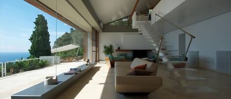 Un espacio habitable moderno con una escalera, un sofá y vistas al mar.