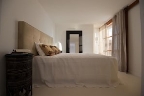 Une chambre avec un grand lit, une table de chevet, un miroir et une fenêtre avec des rideaux.