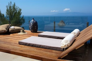 Eine Holzterrasse mit zwei Liegestühlen, einer dekorativen Vase und Blick auf das Meer.