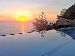 Ein freier Blick auf einen Sonnenuntergang über dem Meer, einen Swimmingpool und eine Steinmauer mit Vegetation.
