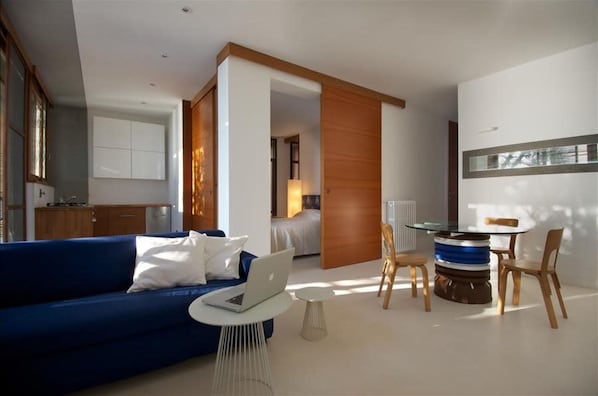 Un salon moderne avec un canapé bleu, un ordinateur portable, une table en verre et des chaises en bois.
