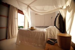 A bedroom with a canopy bed, a bedside table with a book and a hat, and a stack of wooden coasters.