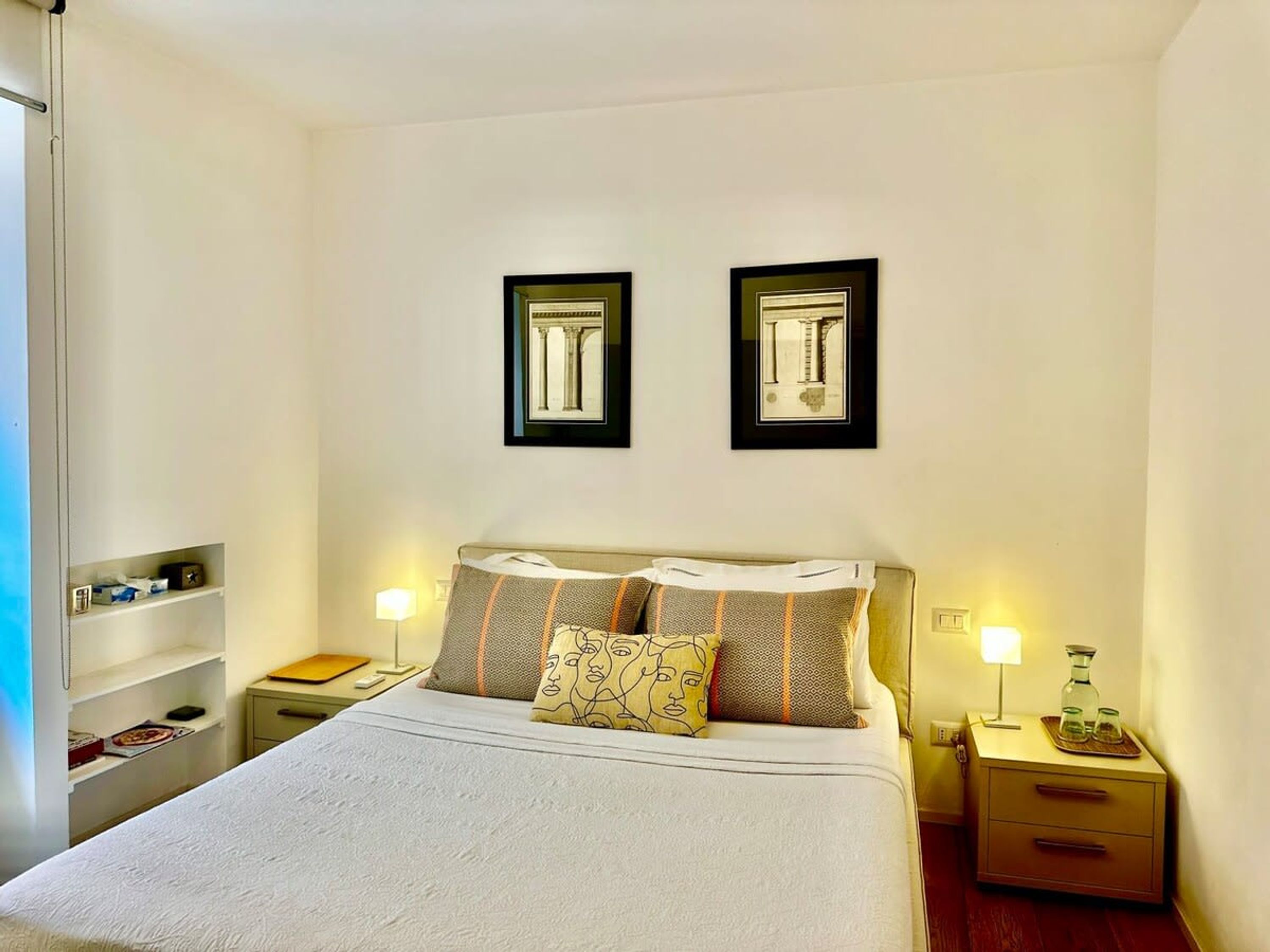 Un dormitorio ordenado con una cama, dos mesitas de noche y dos cuadros en la pared.