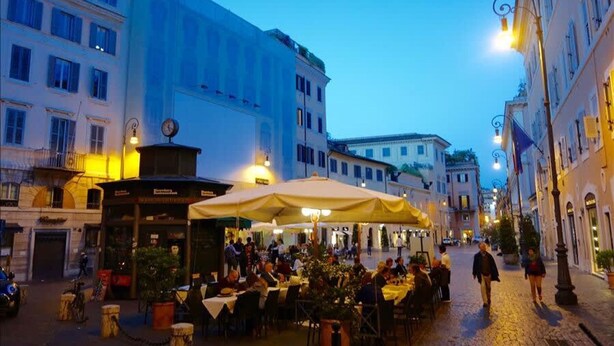 A cobblestone street with outdoor seating at a café, surrounded by historic buildings. - In Rome at Spanish Steps Classy Apartment With Modern Design in an Historic Palazzo (Rome)