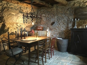 Un intérieur rustique avec un mur en pierre, une table en bois, des chaises et un luminaire suspendu.