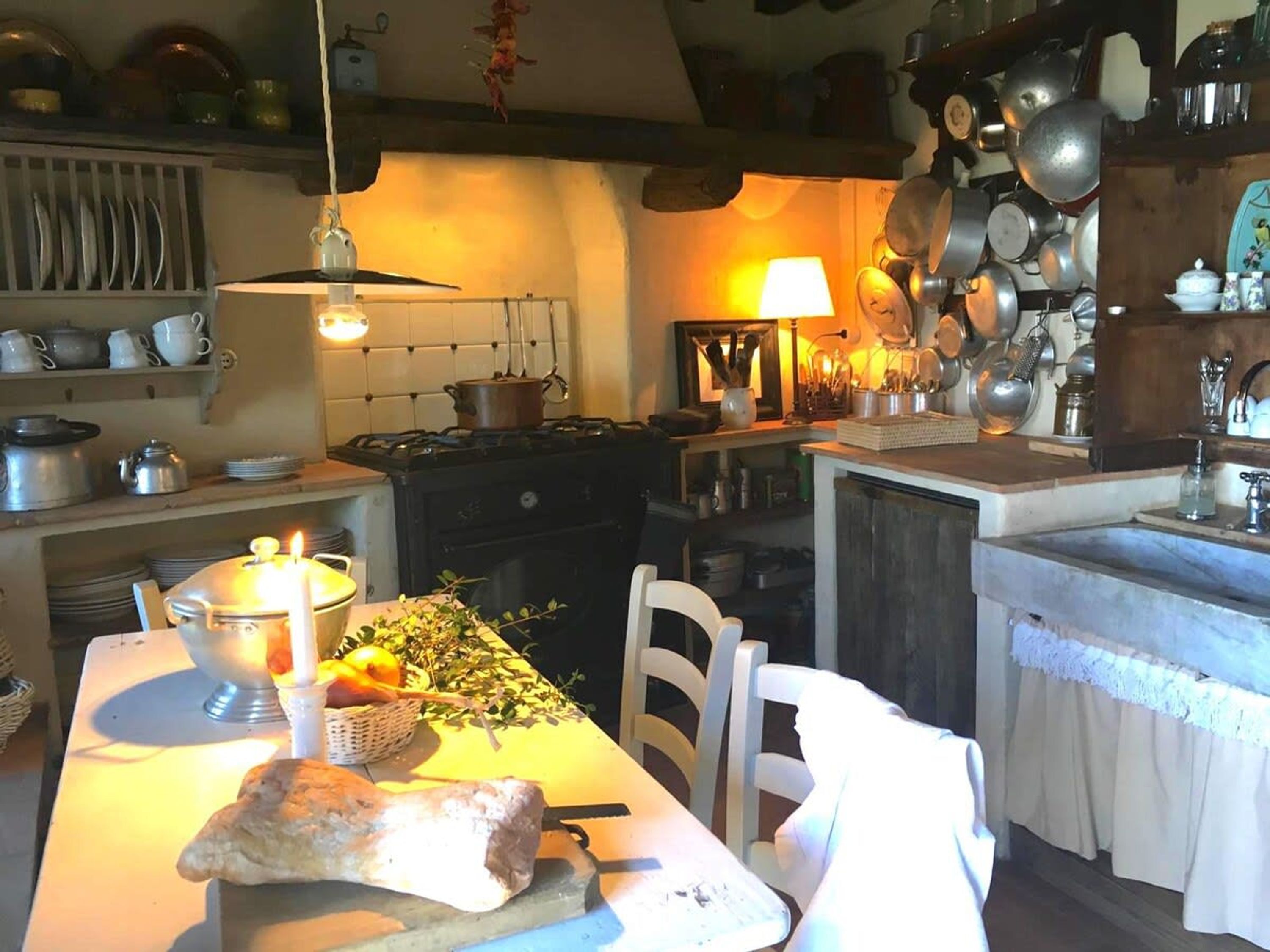 A kitchen with a stove, hanging pots, a table with a candle, and a basket of fruit.