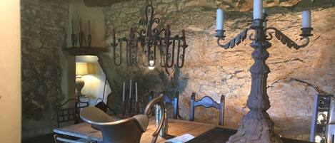 Une pièce rustique avec un mur en pierre, une table en bois, un pichet en métal, un lustre et un chandelier.