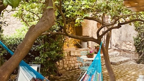 A hammock chair suspended from a tree, a stone wall, and a small round table with a potted plant. - Sermoneta Historic Stone Village House With Pool in a Medieval Hill Town Close to Rome and Naples (Sermoneta)