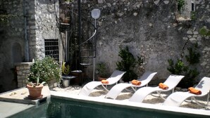 A pool area with white lounge chairs and a stone wall. - Sermoneta Historic Stone Village House With Pool in a Medieval Hill Town Close to Rome and Naples (Sermoneta)