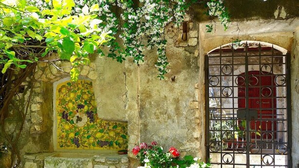 A stone wall with a tiled window, a metal gate, and a potted plant with flowers. - Sermoneta Historic Stone Village House With Pool in a Medieval Hill Town Close to Rome and Naples (Sermoneta)