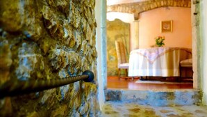 A stone wall with a metal handle, a doorway leading to a room with a table and chairs, and a small table with a vase. - Sermoneta Historic Stone Village House With Pool in a Medieval Hill Town Close to Rome and Naples (Sermoneta)