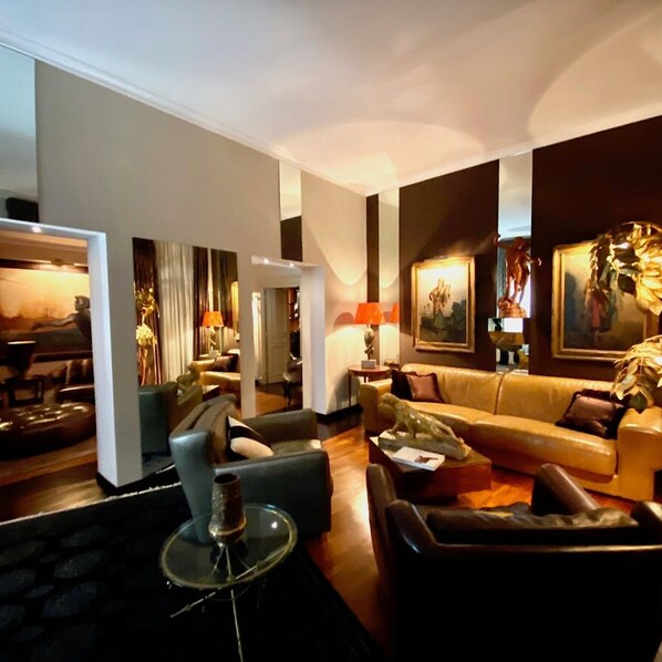 A modern living room with a sofa, armchairs, and a coffee table. There are paintings on the walls and a lamp on a side table. - La Palazzina Santa Dorotea Splendid Rome Townhouse With Courtyard Garden (Rome)