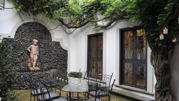 Un cortile con un muro in pietra, una statua, un tavolo con sedie e un albero.