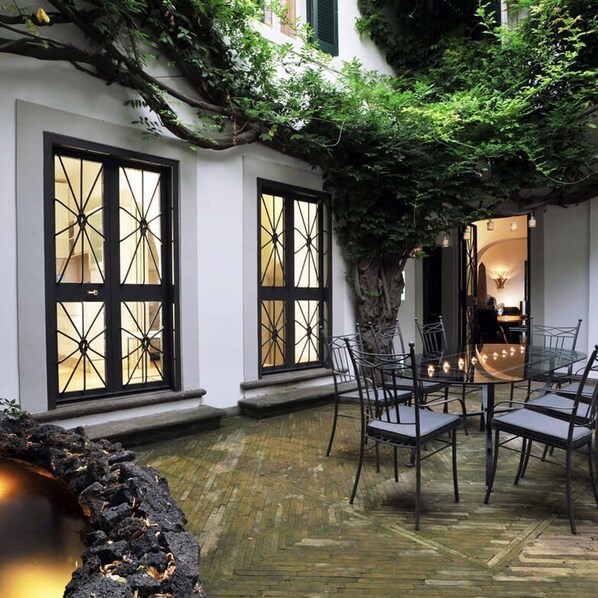 A dining area with a glass table and chairs, surrounded by white walls and large windows with black frames.
