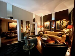 A modern living room with a sofa, armchairs, and a coffee table. There are paintings on the walls and a lamp on a side table. - La Palazzina Santa Dorotea Splendid Rome Townhouse With Courtyard Garden (Rome)