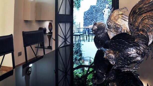A modern interior with a glass partition, a sculpture, and a view of an outdoor garden. - La Palazzina Santa Dorotea Splendid Rome Townhouse With Courtyard Garden (Rome)