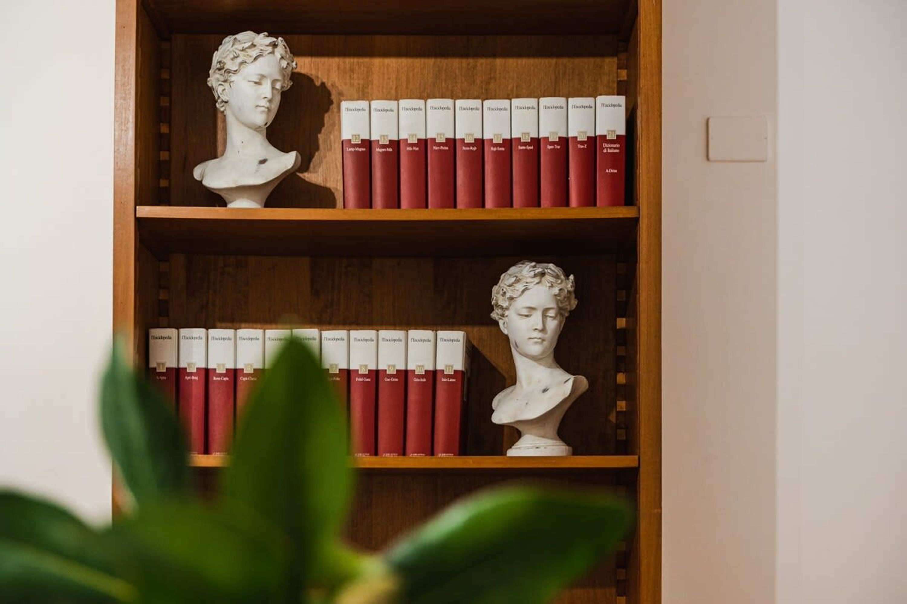 Una estantería de madera con bustos y libros rojos.