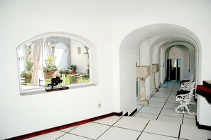 A corridor with white tiled flooring, white walls, and arched doorways leading to another room.