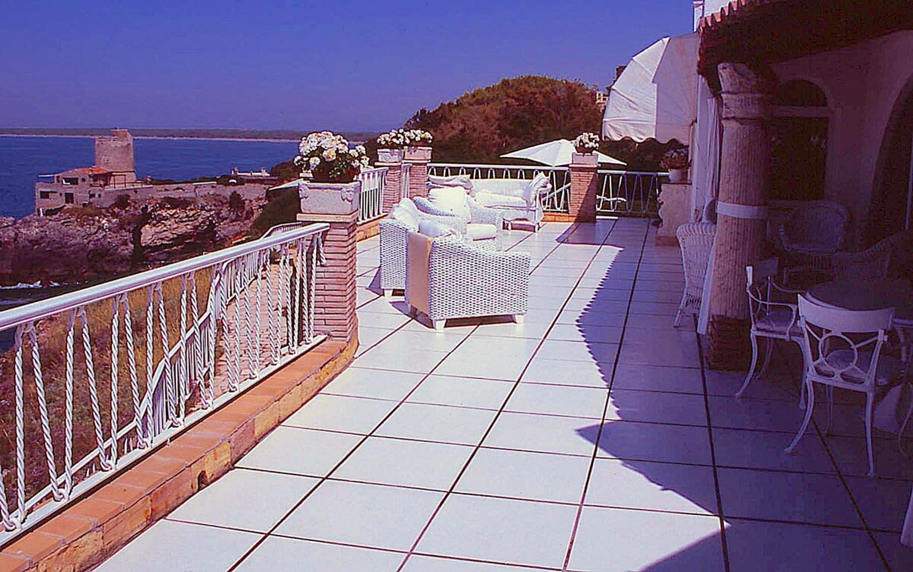 Une terrasse dotée de meubles en osier blanc, d’un sol carrelé et offrant une vue sur la mer.