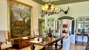 A spacious room with a large painting of a deer, a wooden table, and a chandelier with antlers.