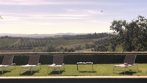 A poolside area with lounge chairs and a view of vineyards and hills.