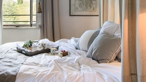 A neatly made bed with a tray of tea and a cake, a map on the wall, and a view of greenery outside.