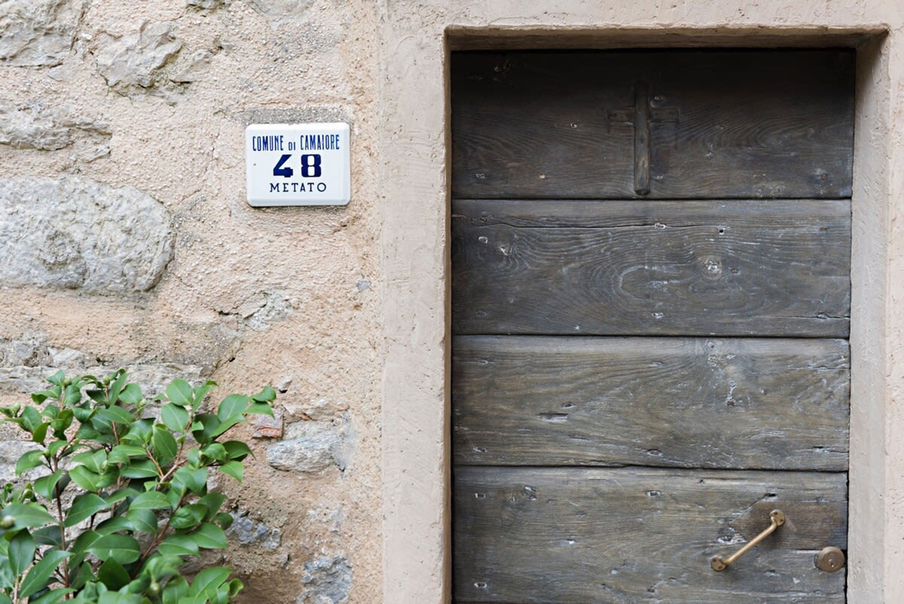 A rustic wooden door with a metal handle, set in a stone wall with a sign above it.