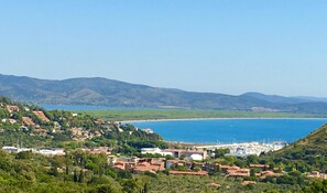 Un pueblo costero con casas escalonadas, un puerto deportivo y una vista despejada del mar y montañas distantes.