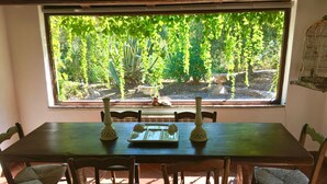A dining area with a large window, a wooden table, and wicker chairs. - Porto Ercole Villa Della Fonte Large Pool Fabulous Sea Views (Monte Argentario)