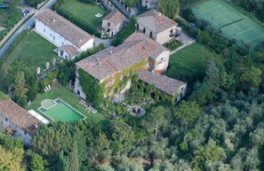 Vue aérienne d’un domaine historique comprenant plusieurs bâtiments, un court de tennis et une piscine.
