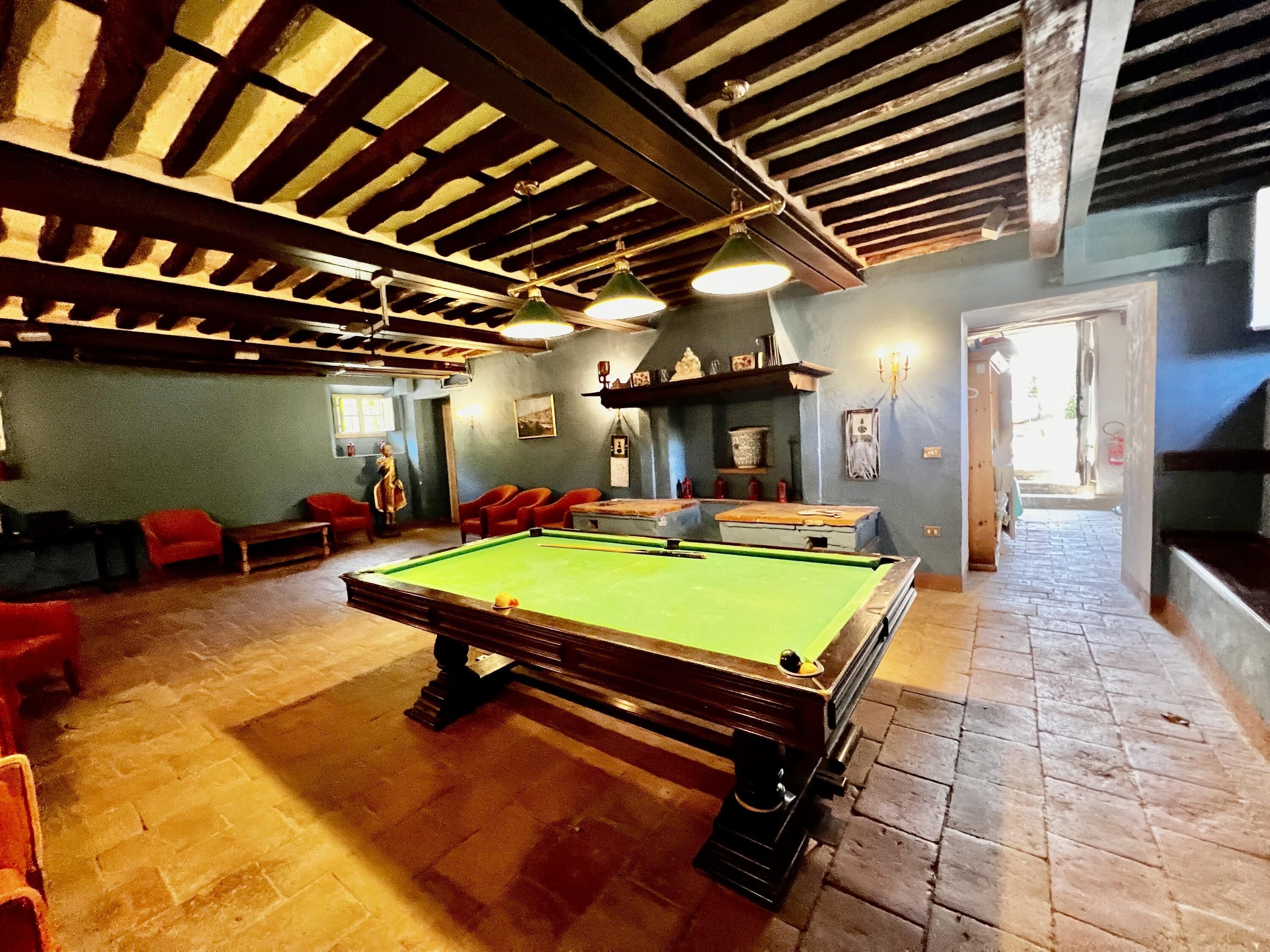 Une salle de billard avec une table de billard, des chaises rouges et un plafond en bois.