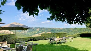 A well-maintained outdoor patio with tables and chairs, surrounded by neatly trimmed hedges and a view of rolling hills. - Villa Vinarte Elegant Home 2 Pools Tennis spa Winery Exclusively for you (Castiglione in Teverina)