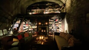 A dimly lit room with a fireplace, a sofa, a coffee table, and a bookshelf filled with books. - Villa Vinarte Elegant Home 2 Pools Tennis spa Winery Exclusively for you (Castiglione in Teverina)