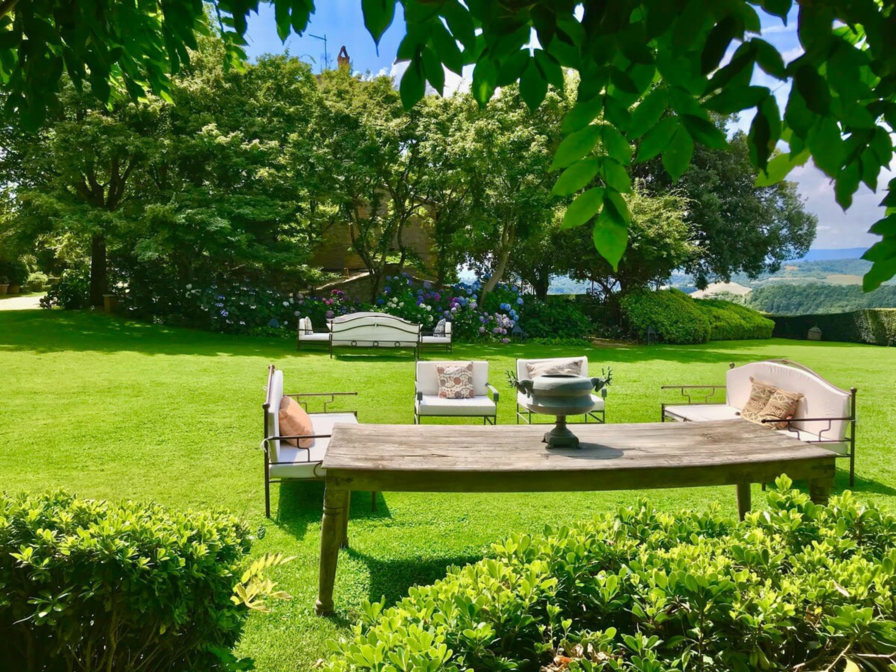 A garden with a wooden table and two white chairs, surrounded by lush greenery and a bench.